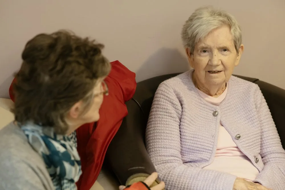 A carer sitting and talking with an older woman in her armchair